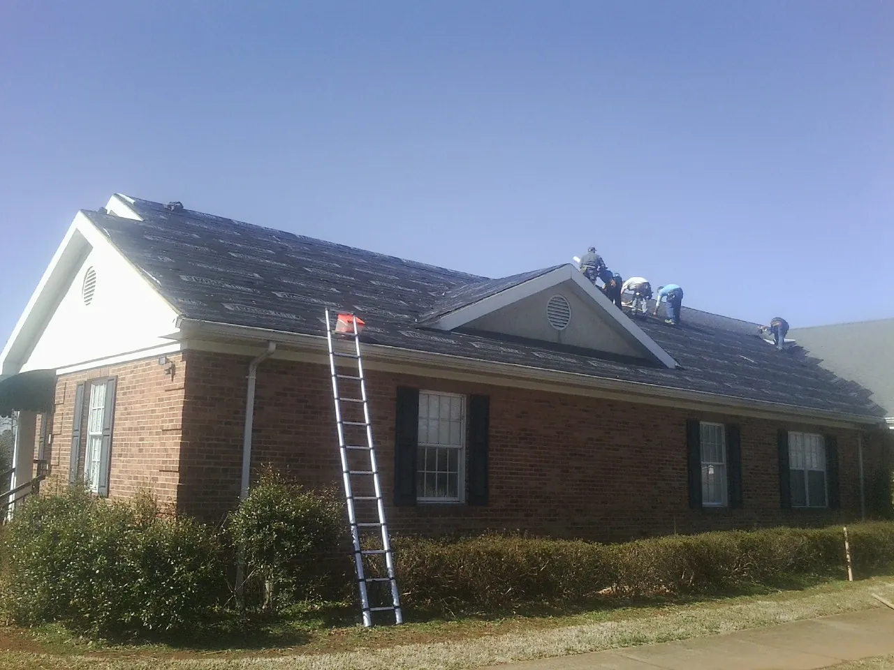 Crew tearing shingles off a brick ranch roof with a ladder set — Emergency Roof Repair work by our crew in New Haven