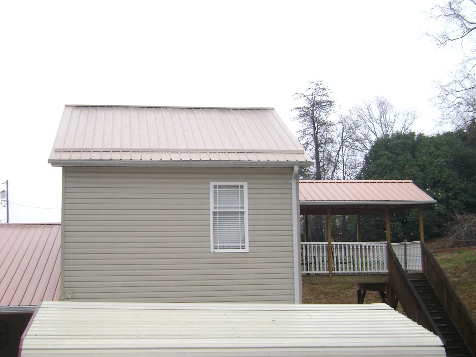 Tan metal roofs on a two story addition and attached porch, from a Roof Replacement job in New Haven
